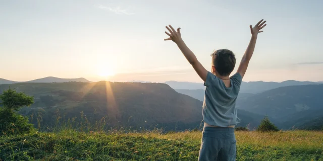 Petit garçon, les bras levés face à un paysage de montagne