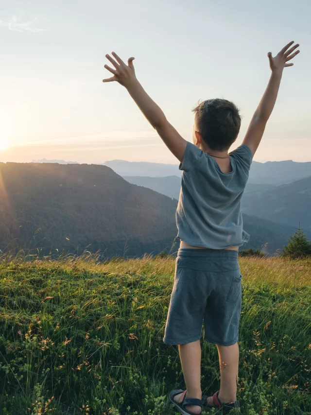 Petit garçon, les bras levés face à un paysage de montagne